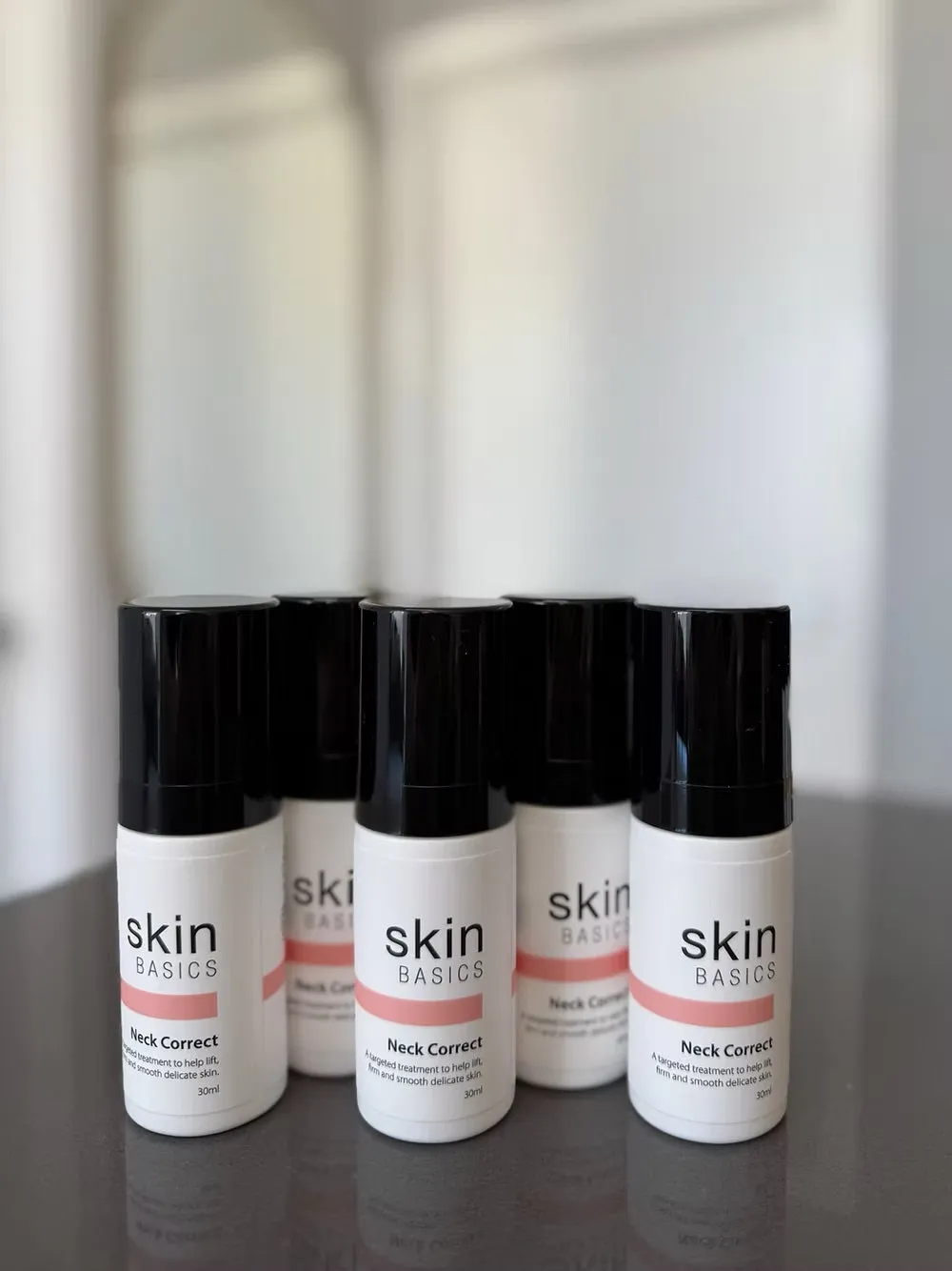 Five white airless bottles of a client's white label Neck Correct with coral label bands, on a dark table