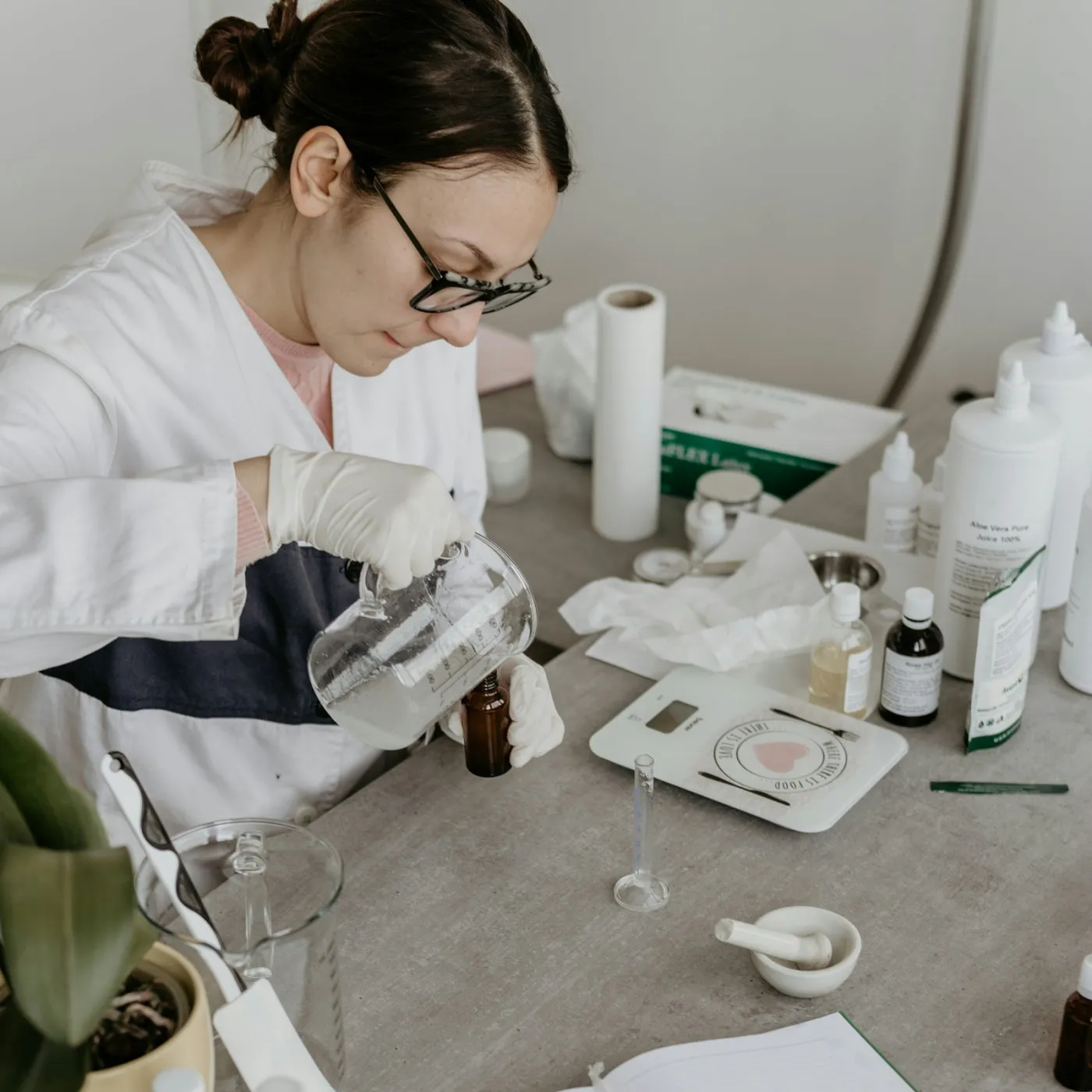 A chemist in a white coat working at a lab bench with glassware